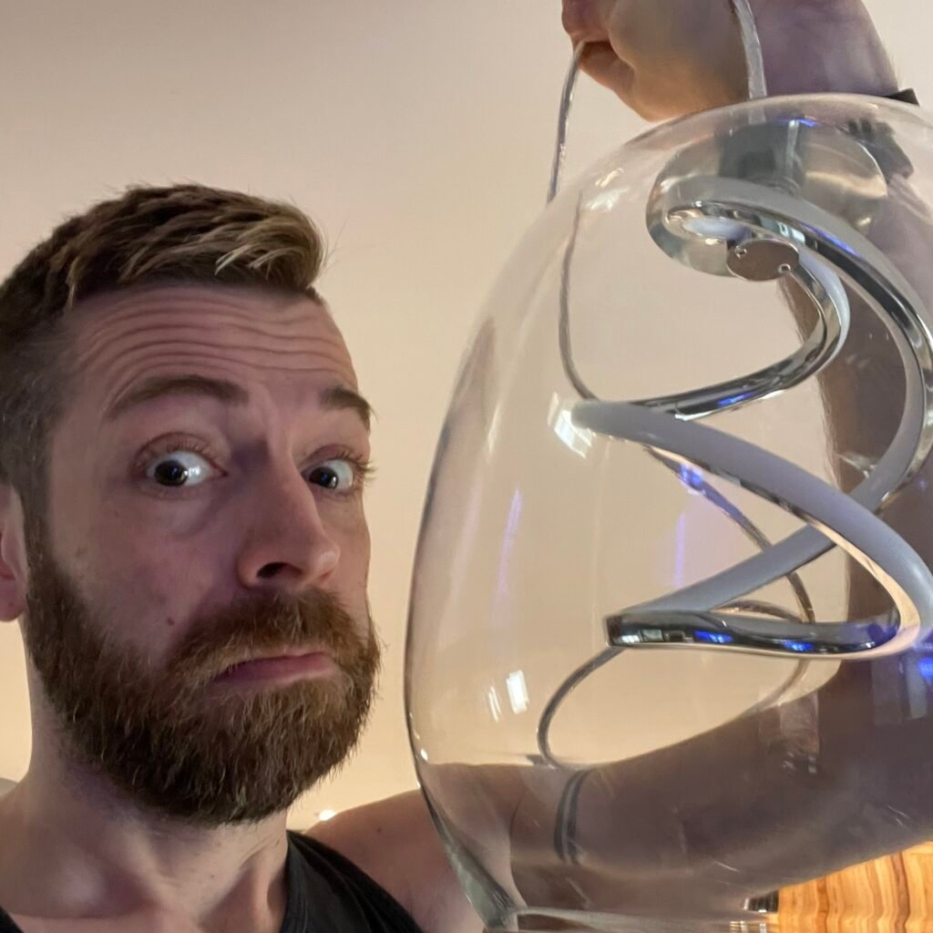 Man holding a modern glass pendant light fixture while repairing or installing it in a kitchen.